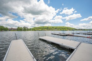 A calm lake with wooden docks extending into the water, surrounded by a lush green landscape and a partly cloudy sky.