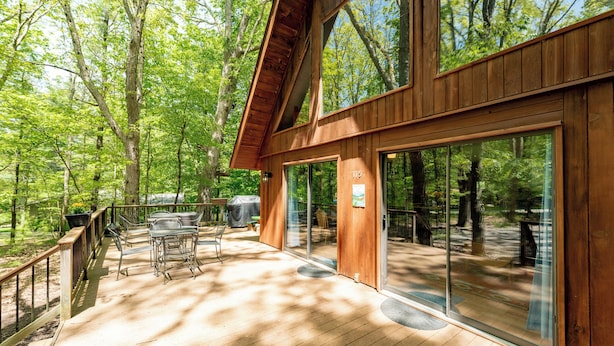 A wooden deck with outdoor furniture, large sliding glass doors, and a view of the surrounding forest. - Woodsy Dog Friendly Retreat w/ Lake Access (SWANTON)