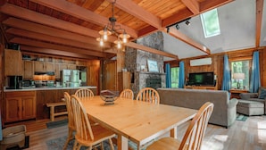 A spacious kitchen with wooden cabinets, a dining table, and a stone fireplace. - Woodsy Dog Friendly Retreat w/ Lake Access (SWANTON)