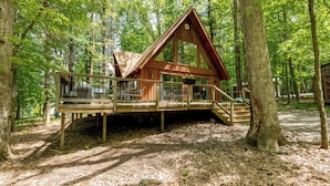 A wooden cabin with a deck, surrounded by trees in a forest. - Woodsy Dog Friendly Retreat w/ Lake Access (SWANTON)