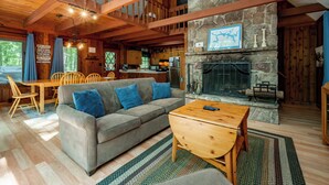 A cozy cabin interior with a stone fireplace, wooden furniture, and a dining area. - Woodsy Dog Friendly Retreat w/ Lake Access (SWANTON)