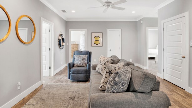 A spacious living room with a grey sofa, a patterned armchair, and a ceiling fan. - Beachfront | Private Heated Pool | Elevator | Pet Friendly (Gulf Shores)