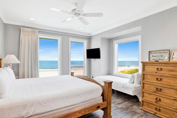 A bedroom with a large bed, a smaller bed, a wooden dresser, a TV, and a view of the beach.