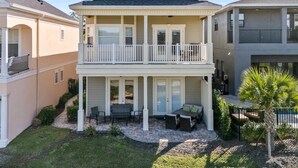 Una casa de dos pisos con balcón, un patio con mobiliario exterior y un jardín bien cuidado.