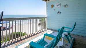 A wooden deck with a view of the beach, a table with chairs, and decorative wall art. - Ocean Dunes 2006 (Kure Beach)