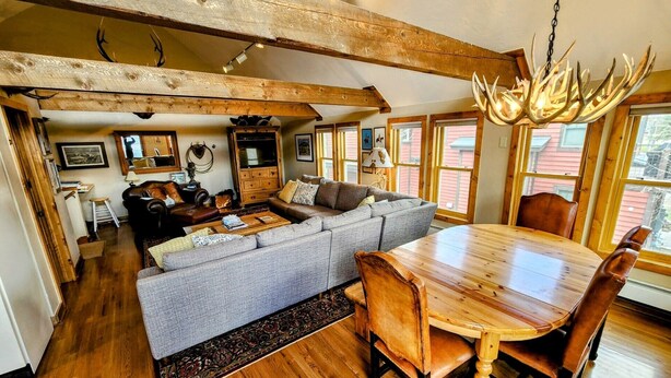 A spacious living room with a wooden dining table, a large sofa, and a chandelier with antlers. - Townhome in Crested Butte | 3 Bedroom | Walk to Elk Ave | Gas Grill | Parking (Crested Butte)