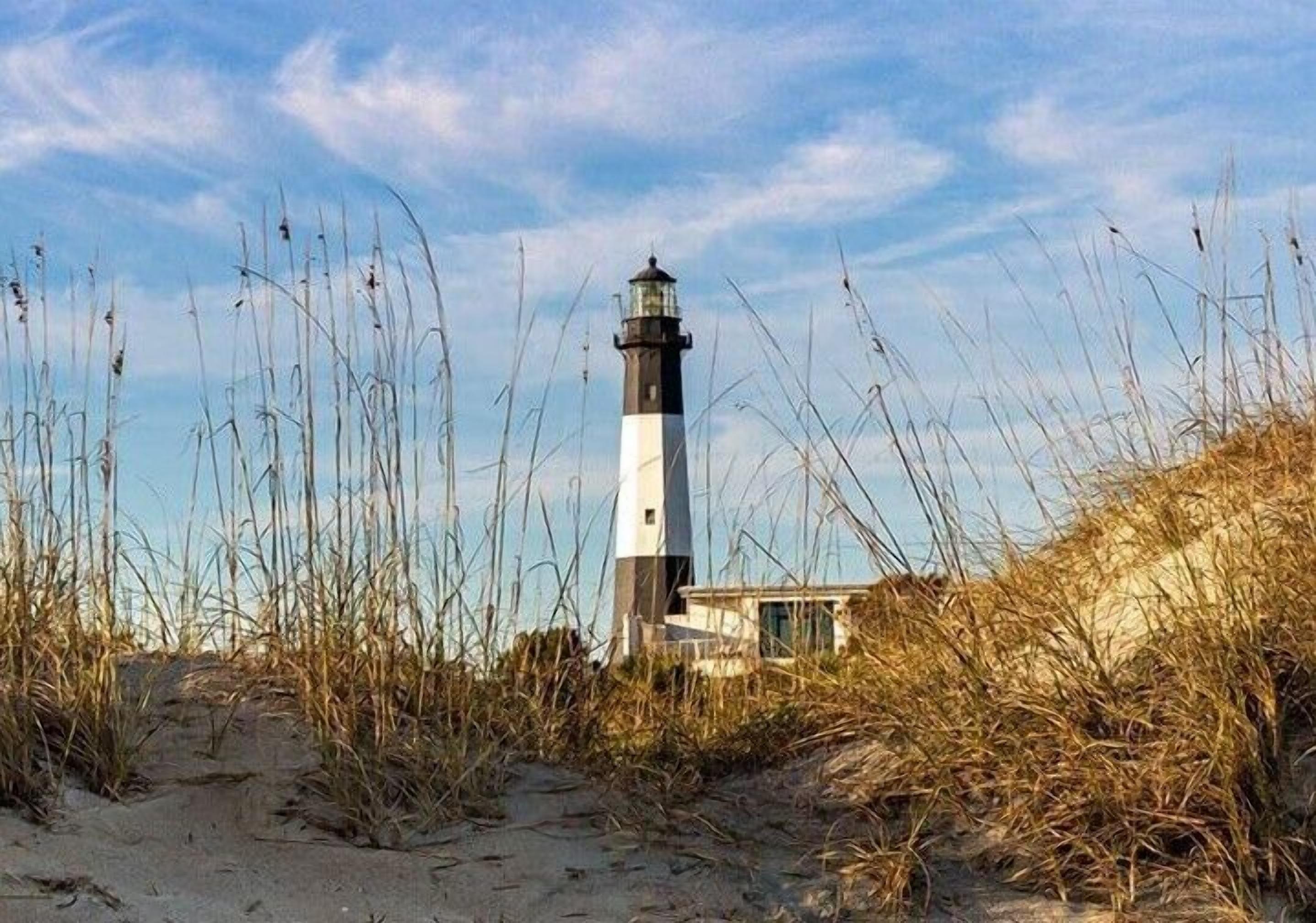 A lighthouse surrounded by tall grass and sand.