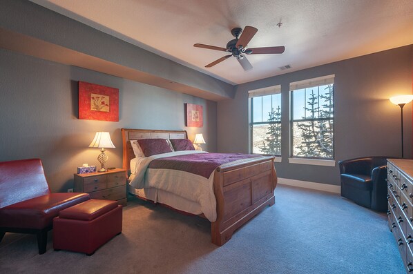 A bedroom with a bed, a chair, a nightstand, a dresser, and a window with a view of trees. - Pine Brook Point T2: 2 bed, 2 bath, quite location (Park City)