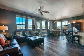 A spacious living room with a dark leather sofa, a dining area with wooden chairs, and large windows offering a view of the outdoors. - Pine Brook Point T2: 2 bed, 2 bath, quite location (Park City)