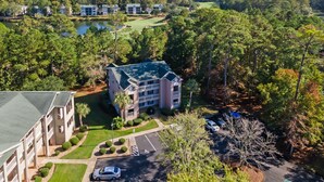 Un hotel de varios pisos con techo verde, rodeado de exuberante vegetación y un campo de golf.