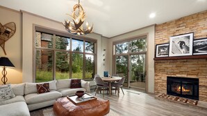 A modern living room with a fireplace, large windows, and a dining area.