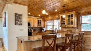 A wooden cabin-style kitchen with a central island, bar stools, and built-in cabinets. - Theater Room,Pool Table,Foosball,HotTub,WiFi,Views (Ferguson)