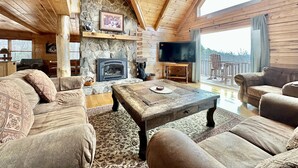 A cozy cabin interior with a stone fireplace, wooden ceiling, and a large TV. - Theater Room,Pool Table,Foosball,HotTub,WiFi,Views (Ferguson)