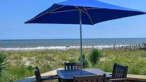 Ein Tisch am Strand mit einem blauen Sonnenschirm, mit Blick auf den Ozean.