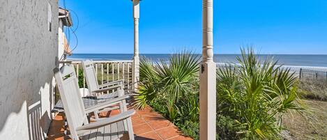 A covered patio with two chairs, a tiled floor, and a view of the ocean.