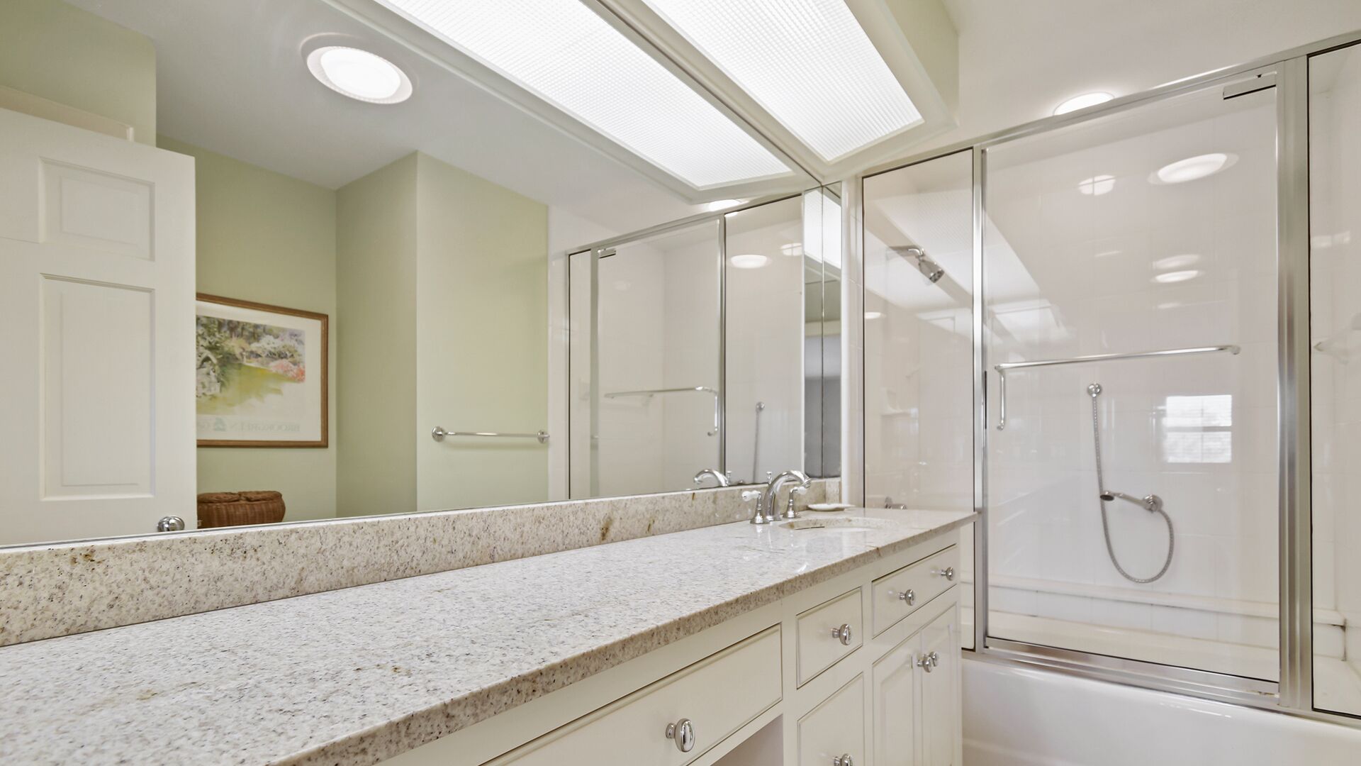 A bathroom with a large mirror, a shower enclosure, and a granite countertop.
