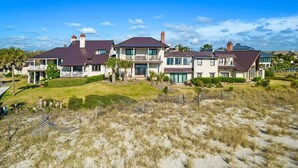 Ein großes, mehrgeschossiges Haus mit weitläufigem Vorgarten und einem sandigen Strand im Vordergrund.