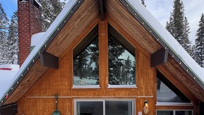 Een houten chalet met een steil dak, grote ramen en een schoorsteen.