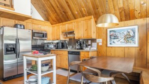 Een moderne keuken met houten kastjes, roestvrijstalen apparatuur, een eettafel en een hanglamp.