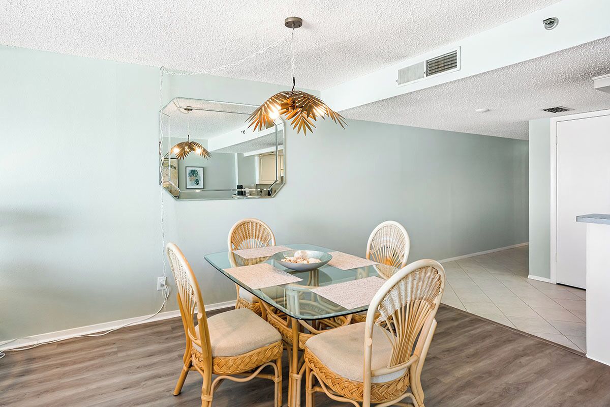 A dining area with a glass table, wicker chairs, and a pendant light.