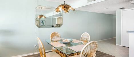 A dining area with a glass table, wicker chairs, and a pendant light.