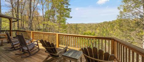 A wooden deck with Adirondack chairs and a table, overlooking a forested area.