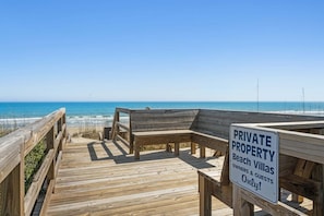 Un paseo marítimo de madera que conduce a villas de playa, con un letrero que indica propiedad privada para dueños e invitados.