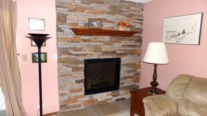 Una sala de estar con chimenea de piedra, un sofá, una lámpara y un cuadro en la pared.