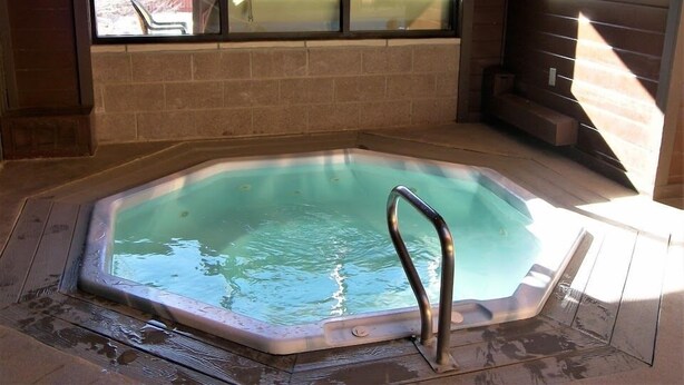 Un jacuzzi con una escalera metálica, un muro de ladrillo y una ventana con vista a un patio trasero.