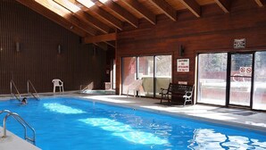 Una piscina interior con agua azul cristalina, paredes de madera y un banco.