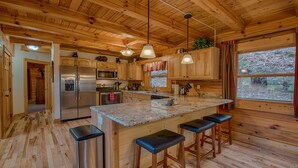 Cocina de cabaña de madera con una isla central, electrodomésticos de acero inoxidable y un amplio ventanal.