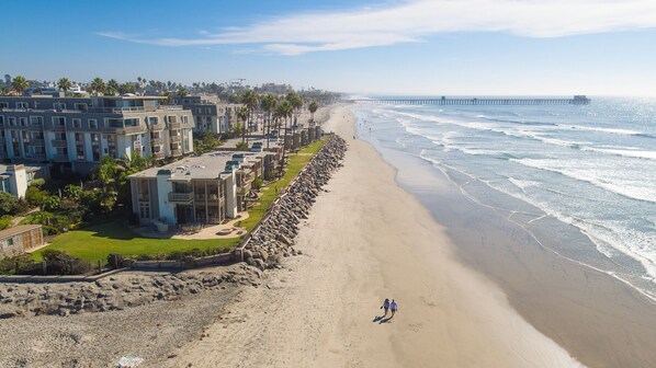 Ein Hotel an der Küste mit mehreren Gebäuden, einem Sandstrand und einem Pier im Hintergrund.