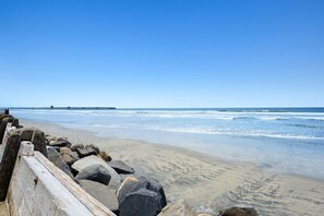 Ein Strand mit einem hölzernen Wellenbrecher und einem Pier im Hintergrund.