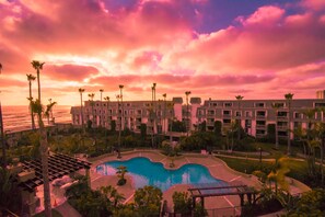 Ein Resort mit Pool, Palmen und Blick auf den Ozean bei Sonnenuntergang.