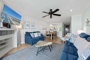 A modern living room with a blue sofa, a coffee table, and a dining area with wooden chairs.