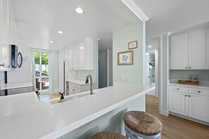A modern kitchen with white cabinetry, a large island with a sink, and two stools.