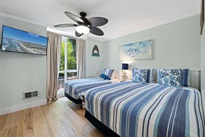 A bedroom with a bed, a ceiling fan, a window with curtains, a wall-mounted TV, and a painting.