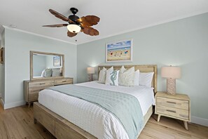 A bedroom with a bed, a nightstand, a dresser, a ceiling fan, and a painting on the wall. - The closest condo to the ocean! New bathrooms, carpet, and furniture! Panoramic ocean views D17 (Oceanside)
