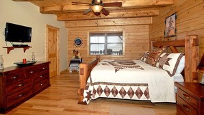 Une chambre située dans une cabane en rondins, avec un lit, une commode en bois, une télévision et un ventilateur de plafond.