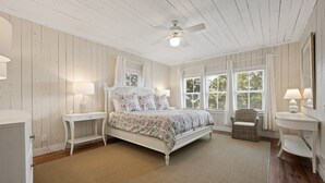 A bedroom with a bed, nightstands, a chair, and a window with blinds. - Eclectic Creek Front Retreat (Georgetown)