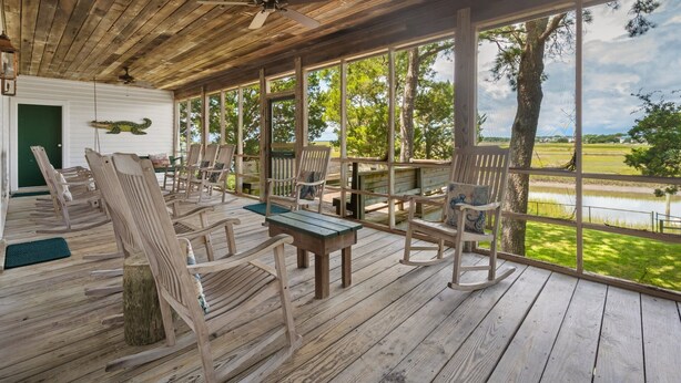 A wooden deck with rocking chairs and a table, overlooking a body of water. - Eclectic Creek Front Retreat (Georgetown)