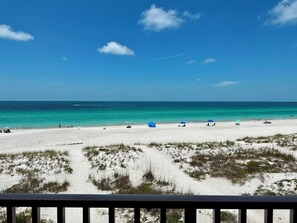A beach with white sand, clear turquoise water, and sparse vegetation.