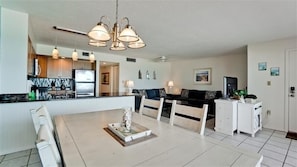 A modern kitchen with a built-in refrigerator, a dining area with a white table and chairs, and a living room with a sofa and a TV. - Coquina Beach Club 202 - Anna Maria Island- Condo 2 Bedroom/ 2 Bath ocean view, maximum occupancy of 6 people. (Bradenton Beach)