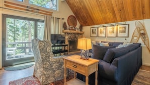 A cozy living room with a large window, a fireplace, a sofa, a TV, and a lamp. - Chalet #14, Great Family Chalet Close the the Main (Mammoth Lakes)