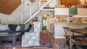 A spacious loft with a high ceiling, a staircase, a cozy living area with a sofa and coffee table, a dining area with a wooden table and chairs, and a kitchen with white cabinets. - Chalet #14, Great Family Chalet Close the the Main (Mammoth Lakes)