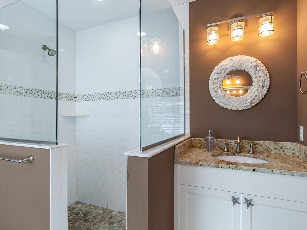 A modern bathroom with a glass shower enclosure, a granite countertop sink, and a decorative wall-mounted light fixture.