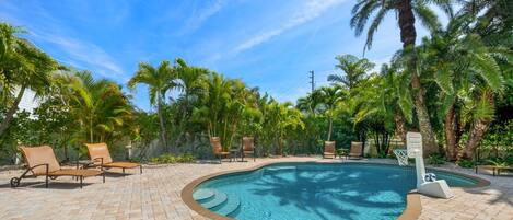 A swimming pool with lounge chairs and palm trees.