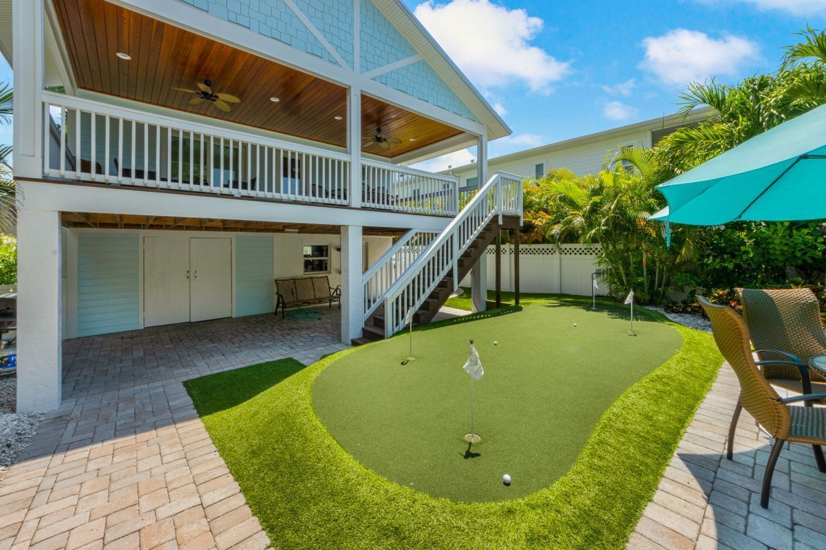 Een tweelaags huis met een overdekte patio, een klein gazon met een golfhindernis en tuinmeubilair.