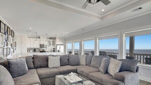 Un salon moderne avec un canapé d’angle, une table basse en verre et une vue sur l’océan grâce à de grandes fenêtres.