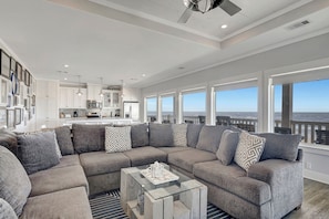 A modern living room with a sectional sofa, a glass coffee table, and a view of the ocean through large windows.